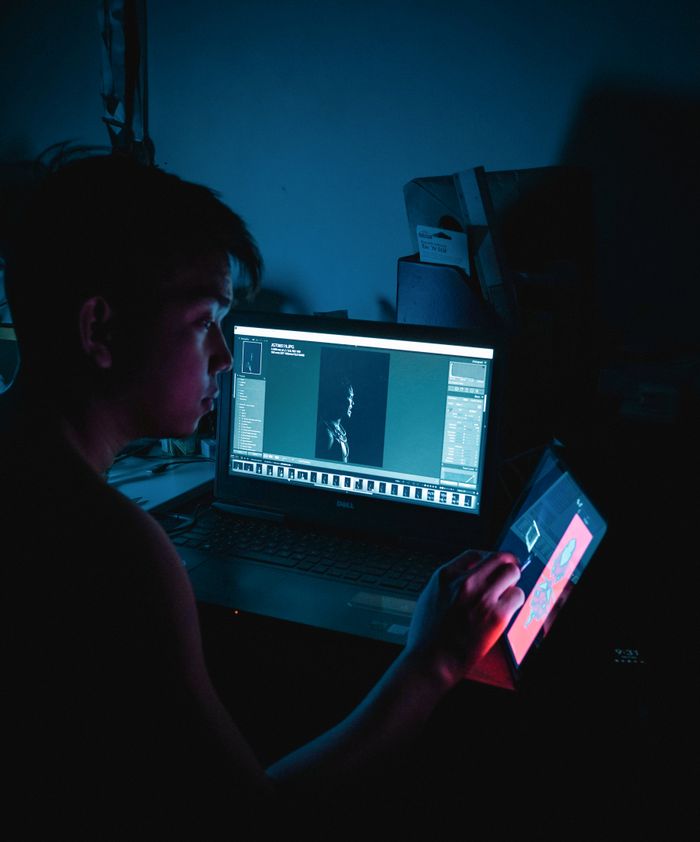 An adult man creating digital art on a touchscreen device in a dimly lit room.
